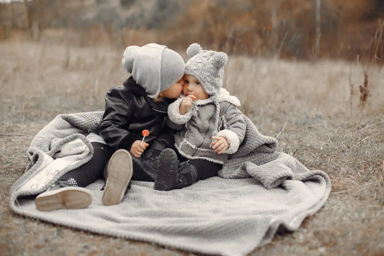 Deux enfants en vêtements d'hiver partageant un moment tendre sur une couverture.